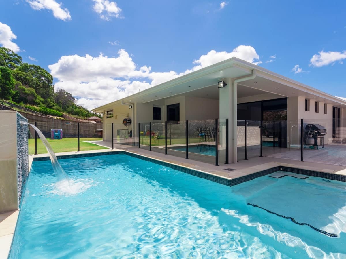 A modern Australian home features a backyard swimming pool surrounded by a glass pool fence, exemplifying the standard of pool fence regulations in the country.