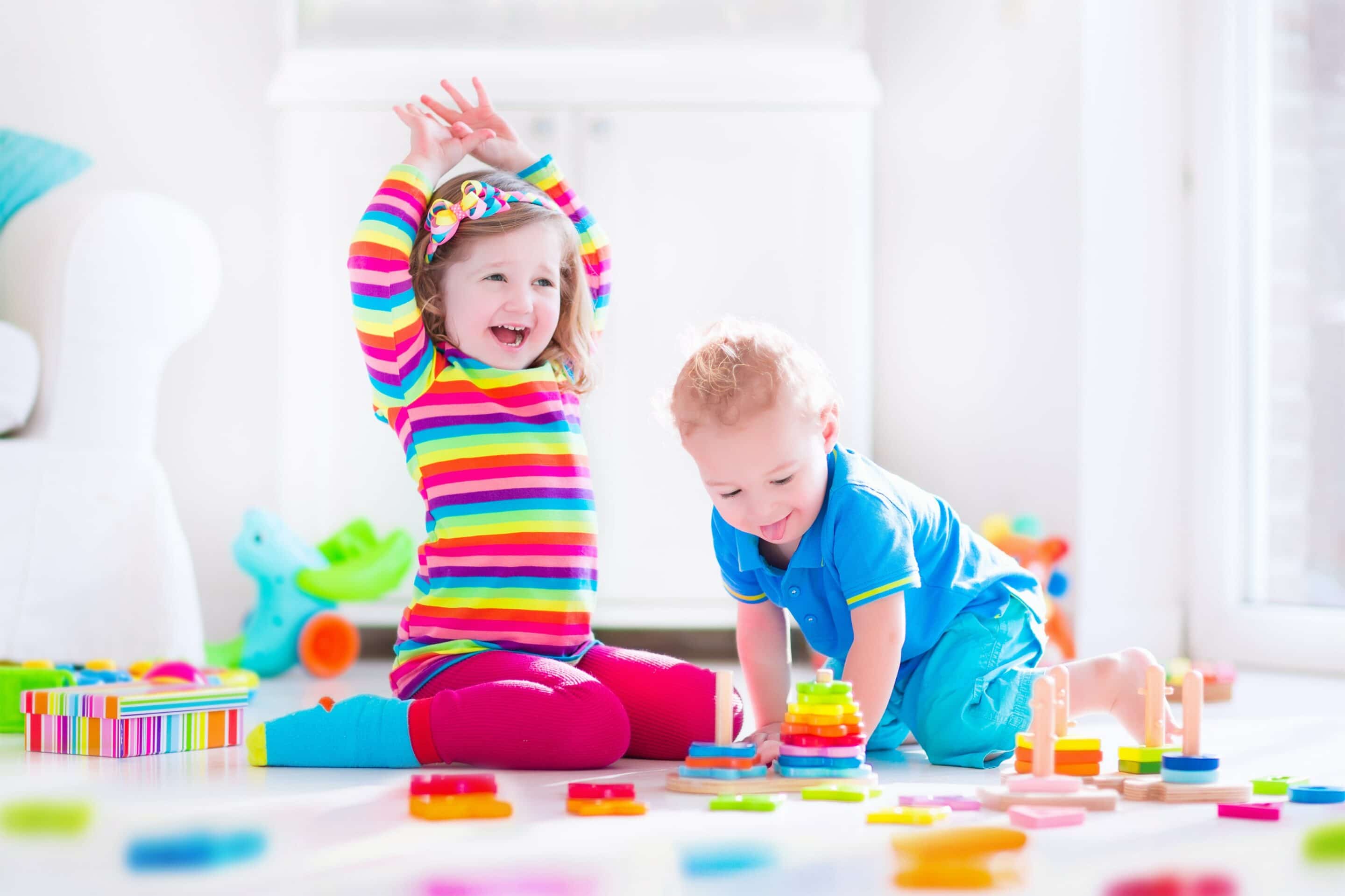 Two young children playing on a mat with coloured blocks.