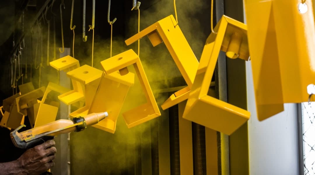 Image showing metal components hanging with a yellow powder coating being applied.