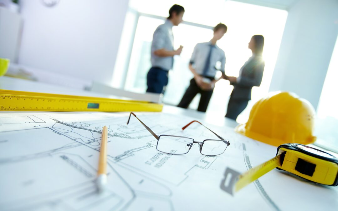 Close up of construction planning papers with three people having a meeting in the background.