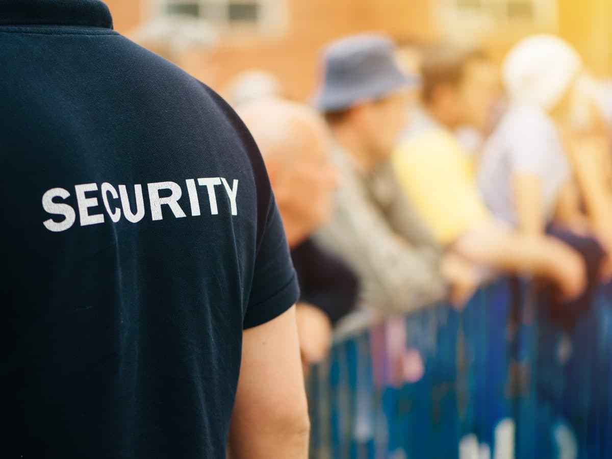 Security guard and crowd behind a pedestrian barrier at an event.