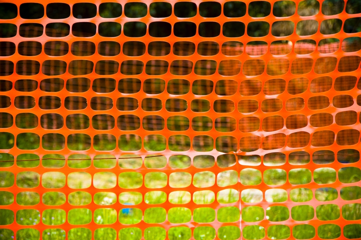 Orange plastic mesh fencing installed in a garden to protect lawn.