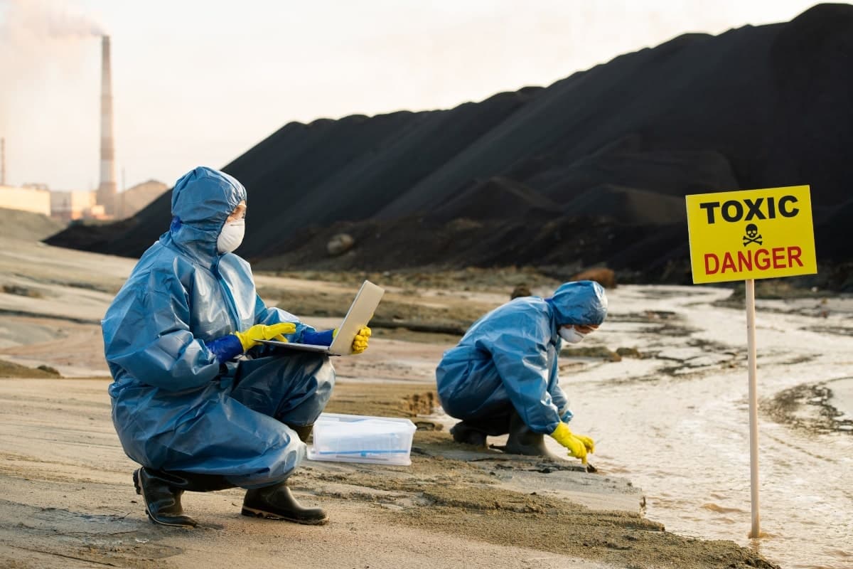 Two scientists in protective gear testing waterway contaminated by sediment flow. 