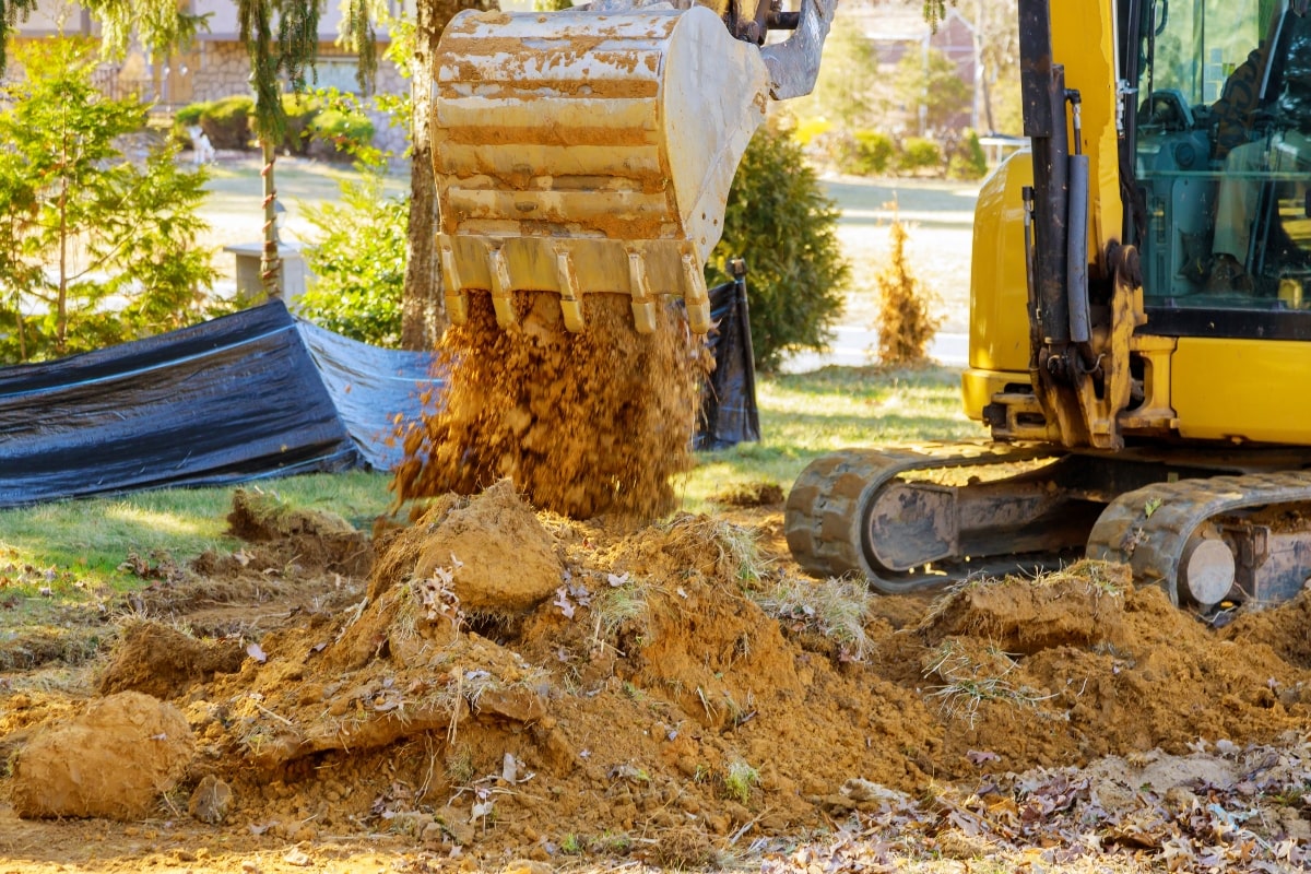 An excavator digging up soil next to a sediment control fence.