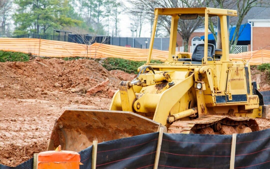 Excavator on a construction site, with silt fencing installed to control sediment flow.