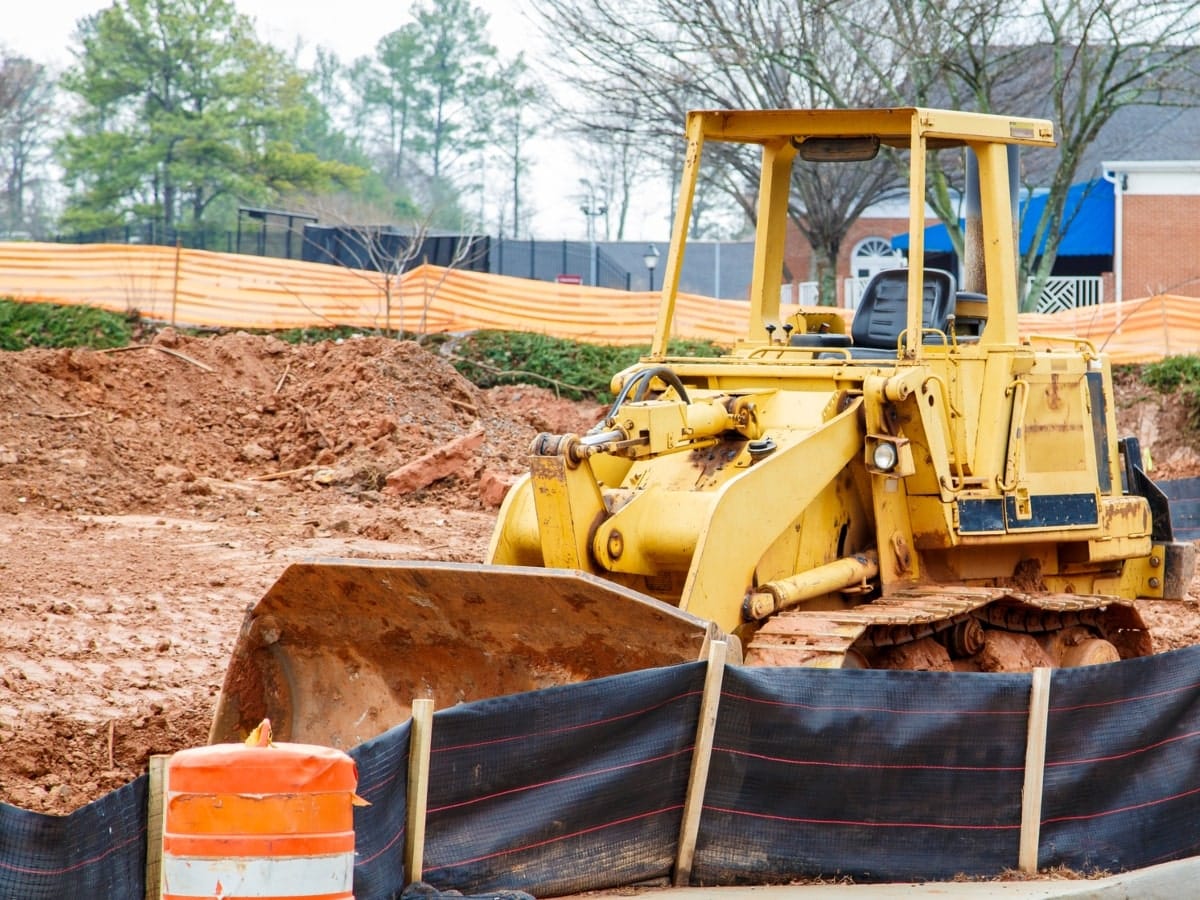 Excavator on a construction site, with silt fencing installed to control sediment flow.