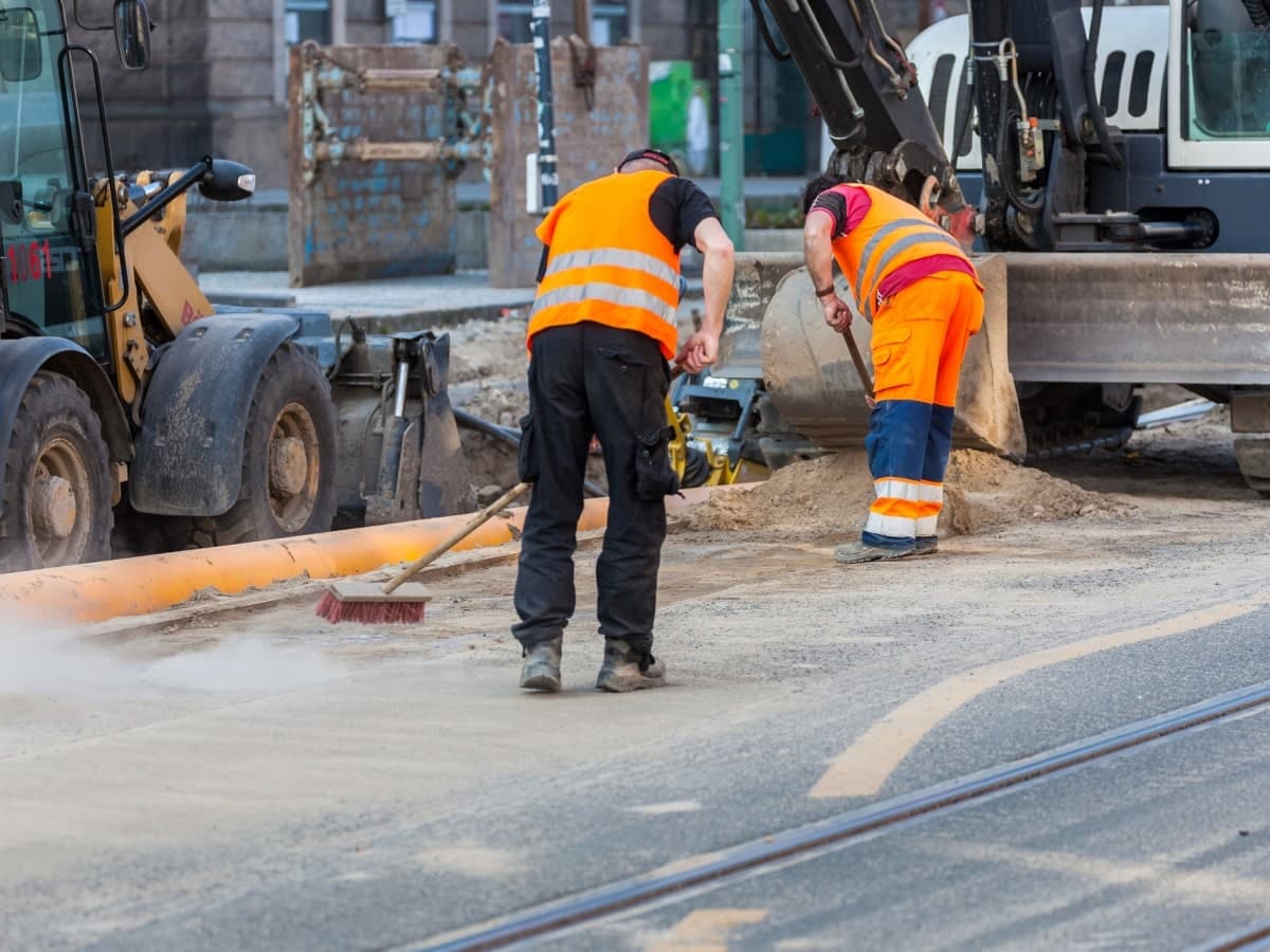 Workers on a construction site using brooms to keep the area clean and tidy.