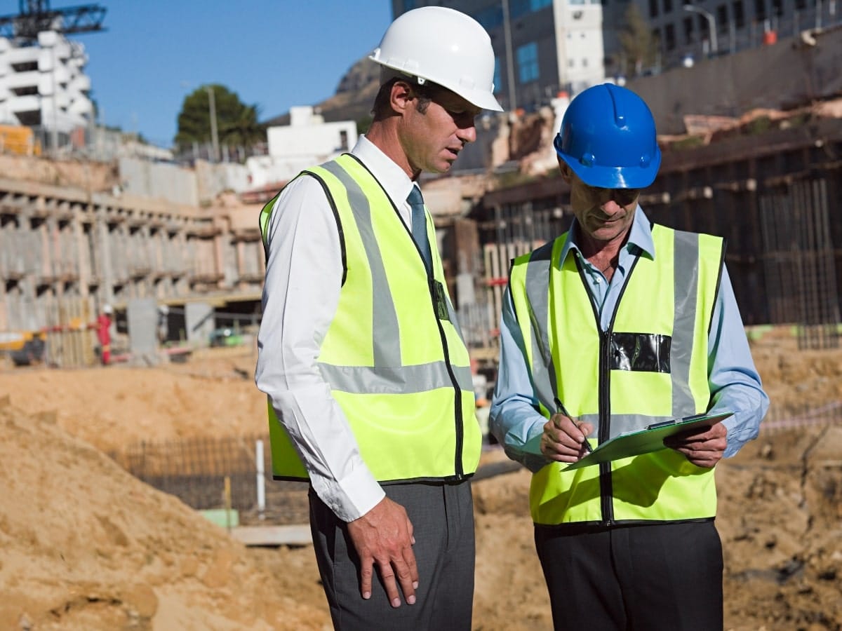 Large construction site with two managers in high vis and hard hats discussing workplace safety.