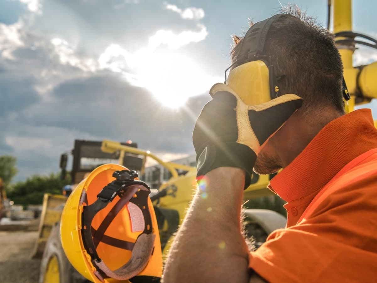 A worker wearing personal protection equipment (PPE) ear muffs on a construction site to protect against noise-induced hearing loss. 