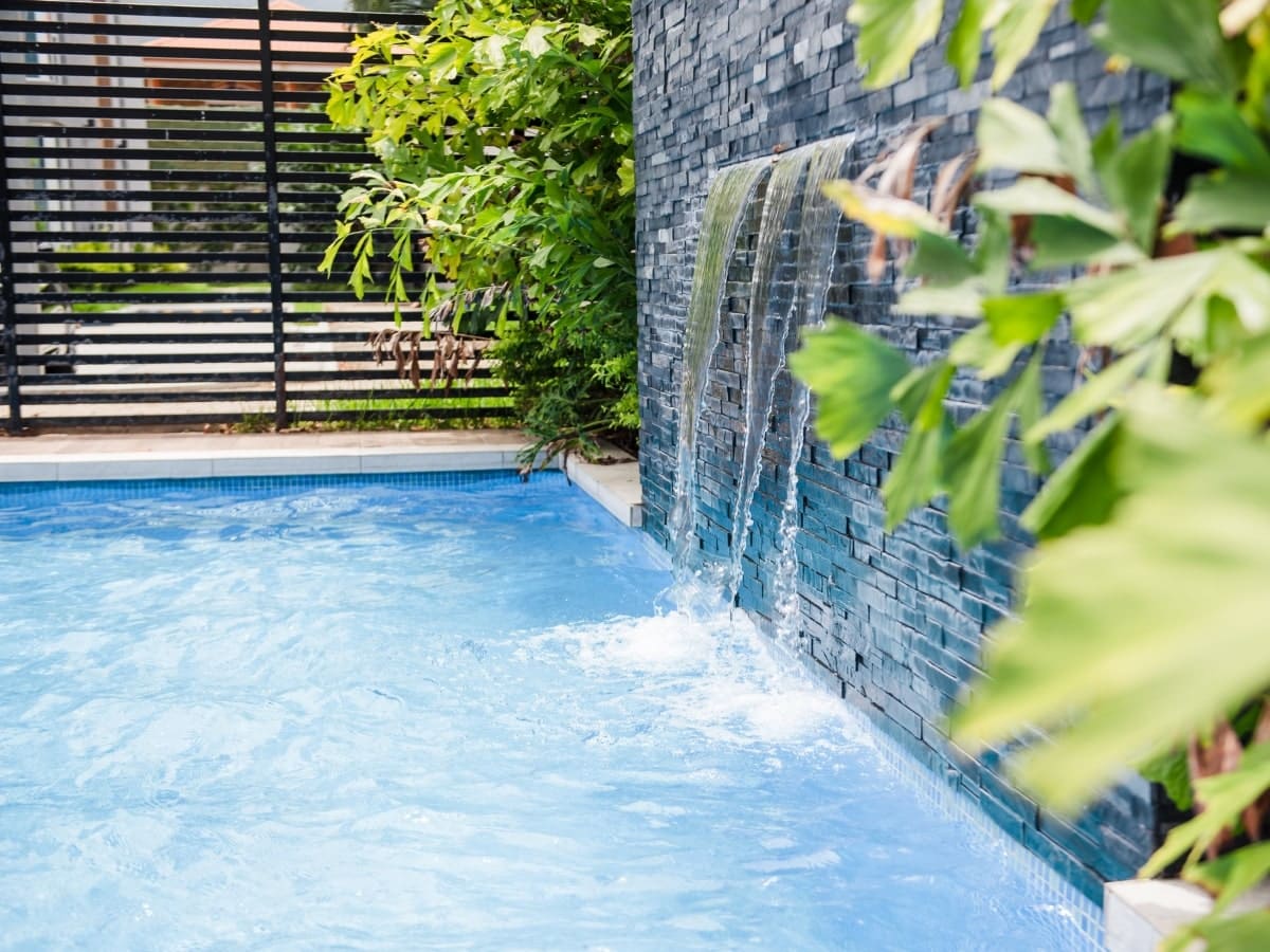 Lush garden setting featuring a pool with a cascading water feature and custom pool fencing, representing one of the unique types of pool fences available.