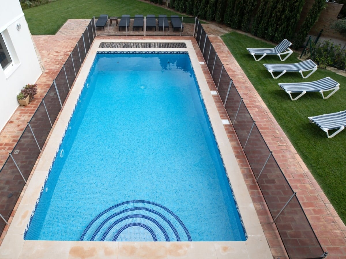 Bird's-eye view of a swimming pool bordered by decorative fencing with distinct perforated mesh design, highlighting innovative types of pool fences for modern homes.