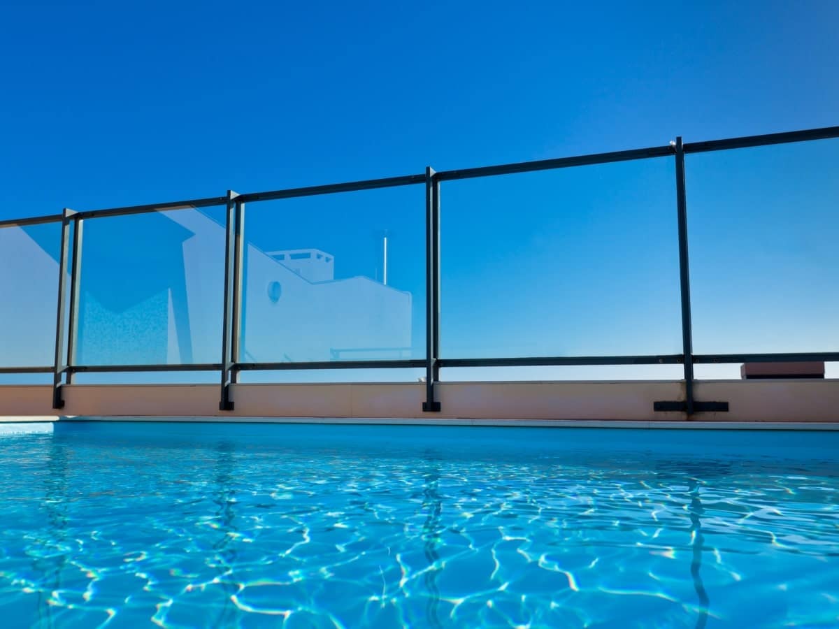 Outdoor pool bordered by framed glass fencing, highlighting one of the distinct types of glass pool fencing with a clear blue sky backdrop.