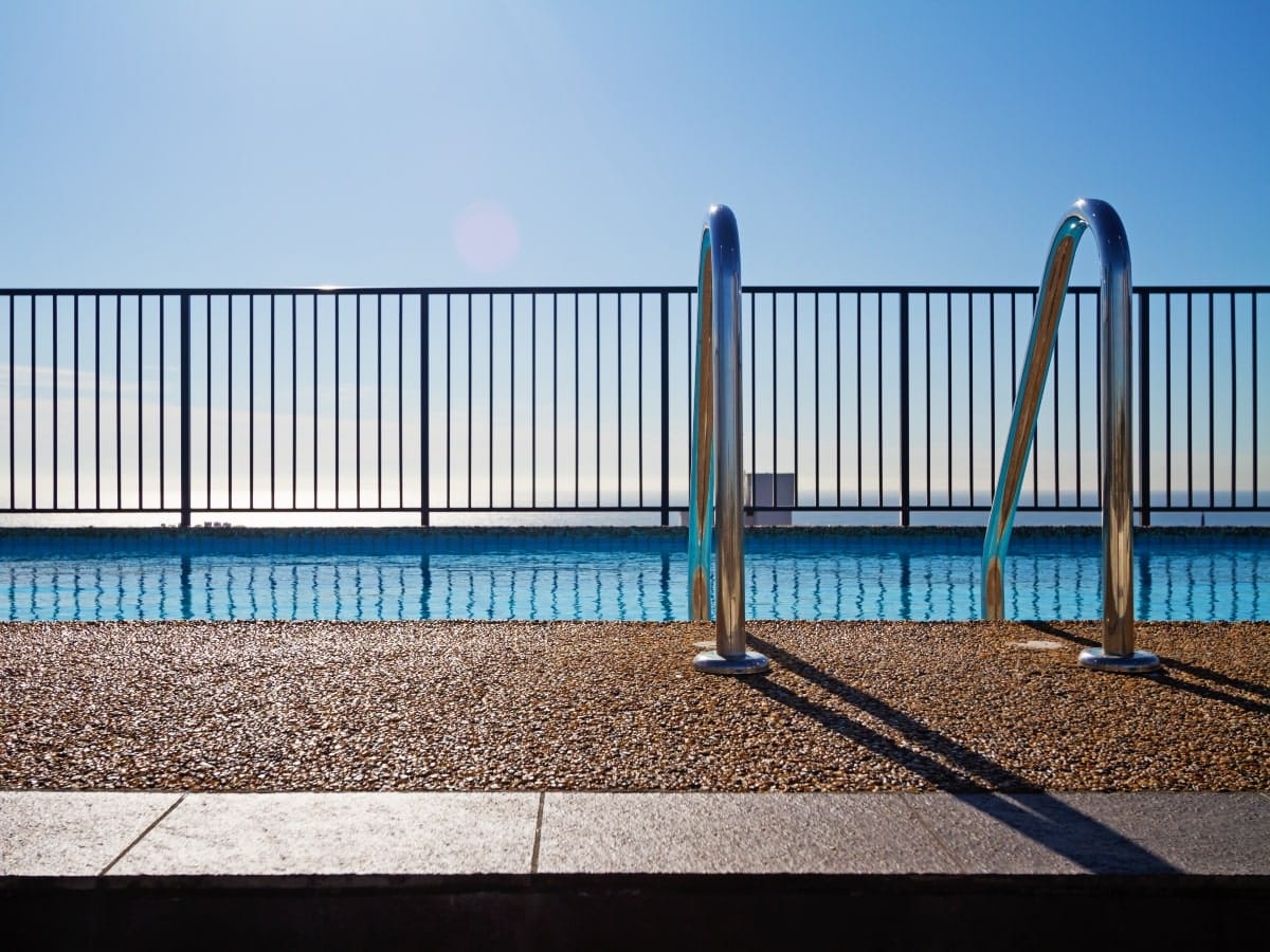 Outdoor swimming pool bordered by a metal fence with spaced bars, exemplifying traditional and functional pool fencing types.