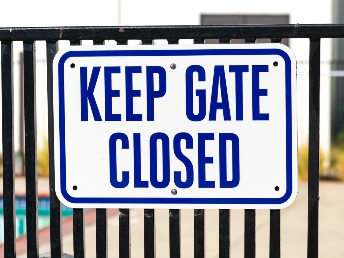 A prominent sign displaying the words 'Keep Gate Closed', attached to a fence with a pool in the background.