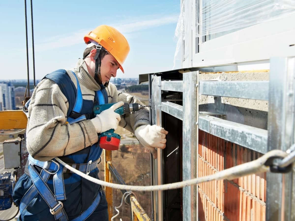A construction worker with safety harness and helmet is securing edge protection barriers on a roof, showcasing the implementation of roof edge protection measures to ensure site safety.