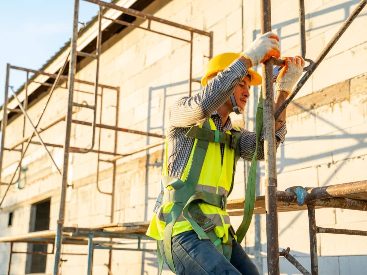 A construction worker clad in a high-visibility vest and safety helmet on a scaffold, highlighting safety on the job site.