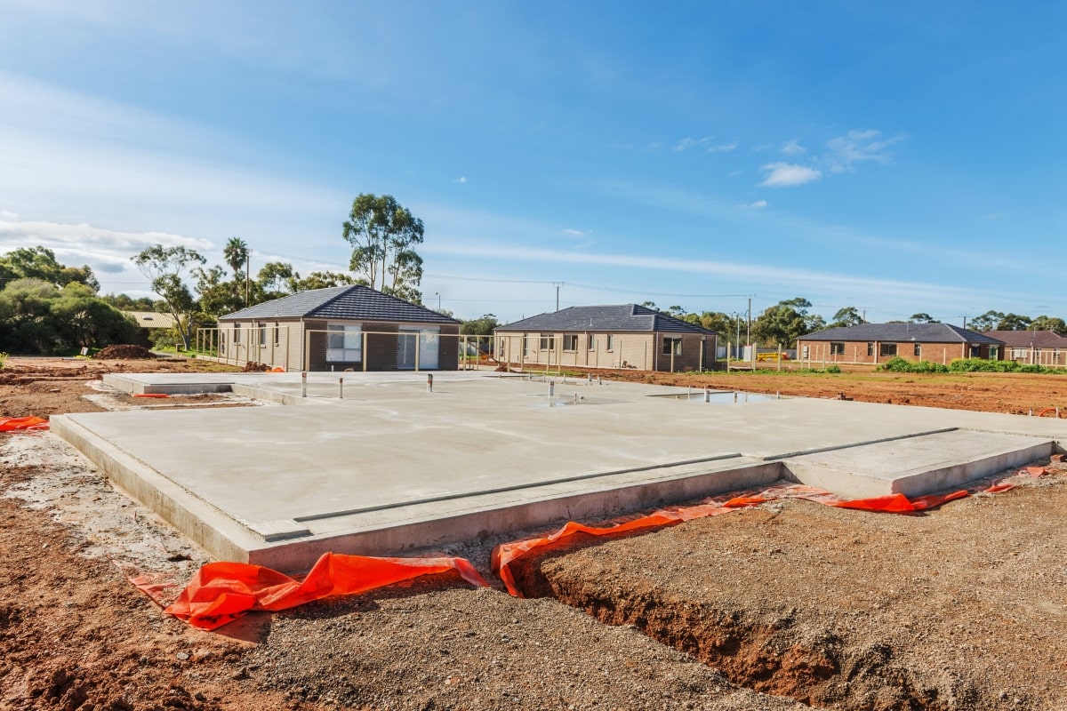 Freshly poured concrete foundation of a new house, with plumbing stubs in place, marking the base stage in the stages of building a house.