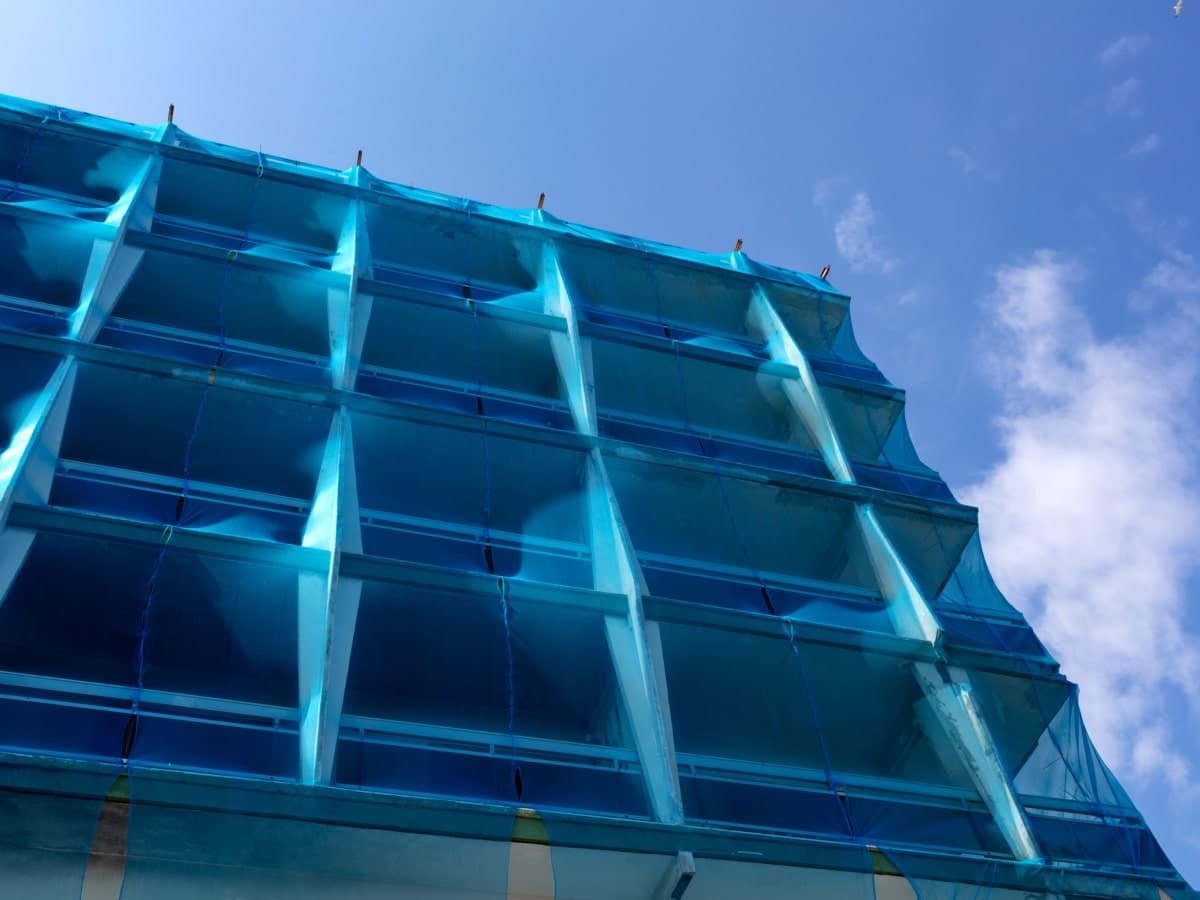 Blue scaffold netting enveloping a building under construction, a control measure in compliance with working at heights regulations.