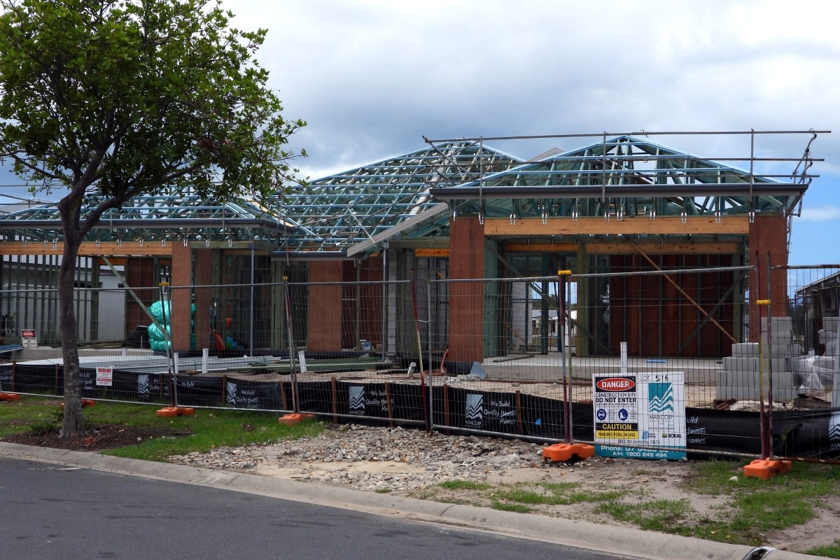 A new house under construction, surrounded by temporary fencing, showcasing the ongoing development from initial planning to the final stage before becoming a home.