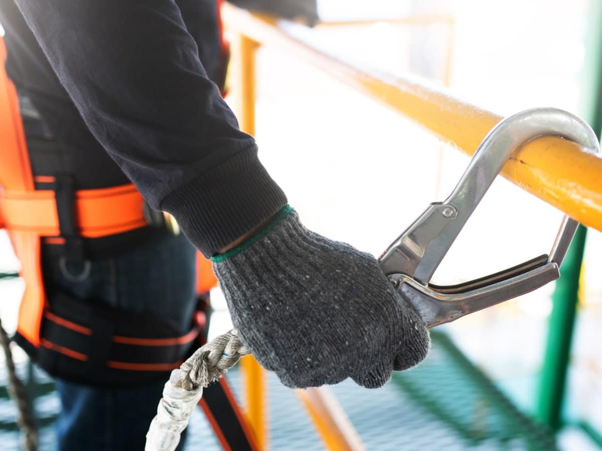 Close-up of a construction worker attaching a safety line to a secure point, demonstrating fall prevention and working safely at heights.