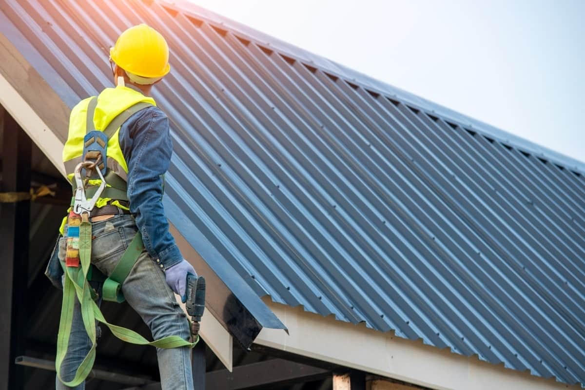 A builder works on attaching a corrugated metal roof to a residential building, highlighting the roofing aspect of the lockup stage in construction.