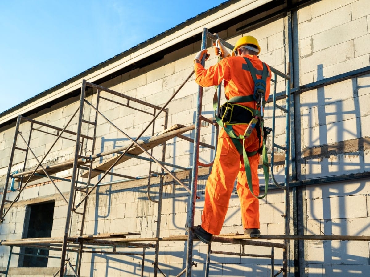 Construction worker secured with a safety harness while working on scaffolding, showcasing regulatory compliance for safe work at heights.