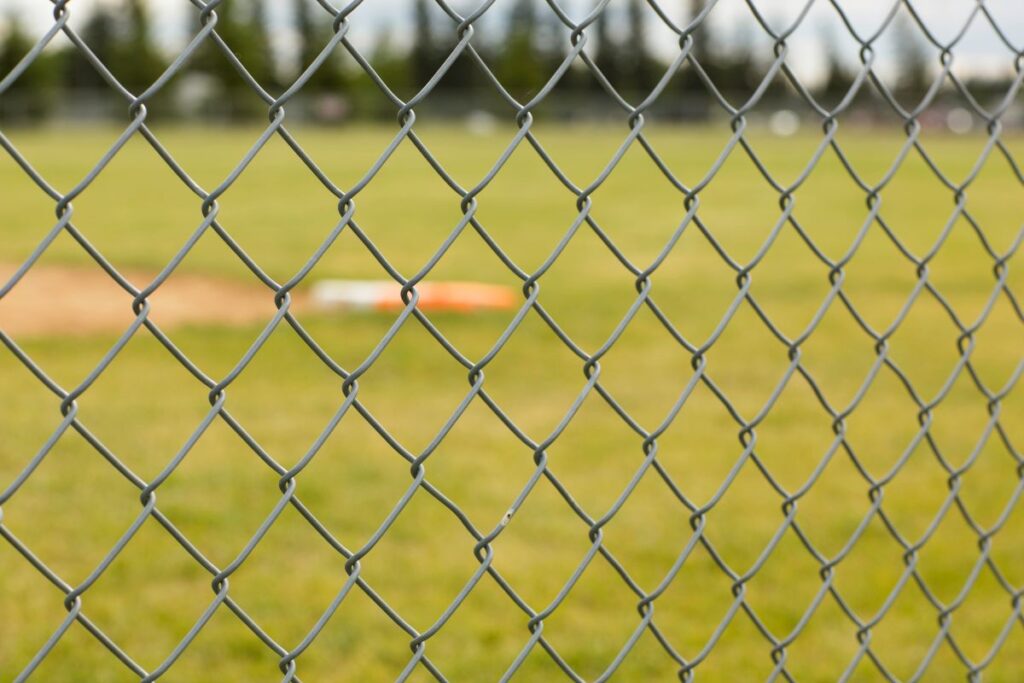 A chain link fence in close up, with blurred sports field in the background.