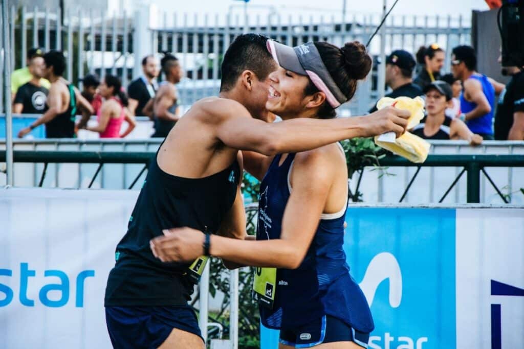 Two competitors congratulate each other, with banner advertising attached to fences in the background.